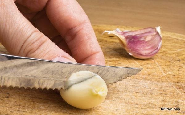 hand slicing garlic cloves on the cutting board with a knife
