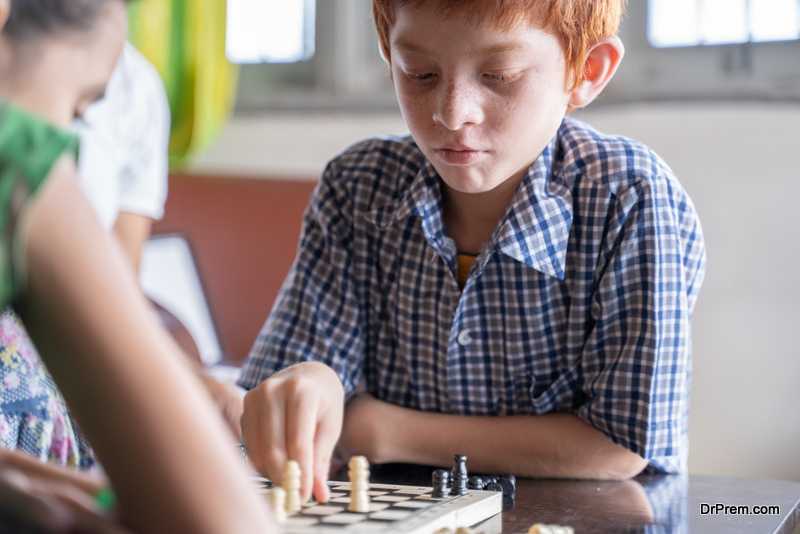 Serious chess player kid thinking and movind coin at home - Concept of kid concentration of game during Early development, home educational games for children.